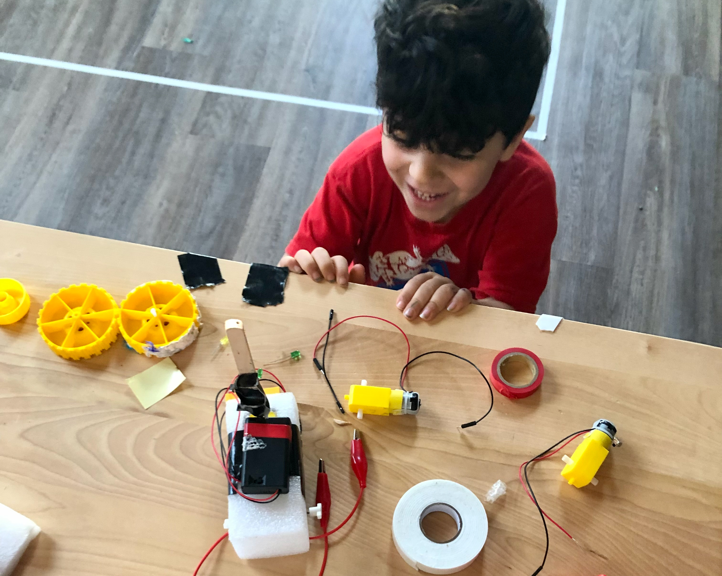 Child building a robot with yellow wheels and wires at Robot School